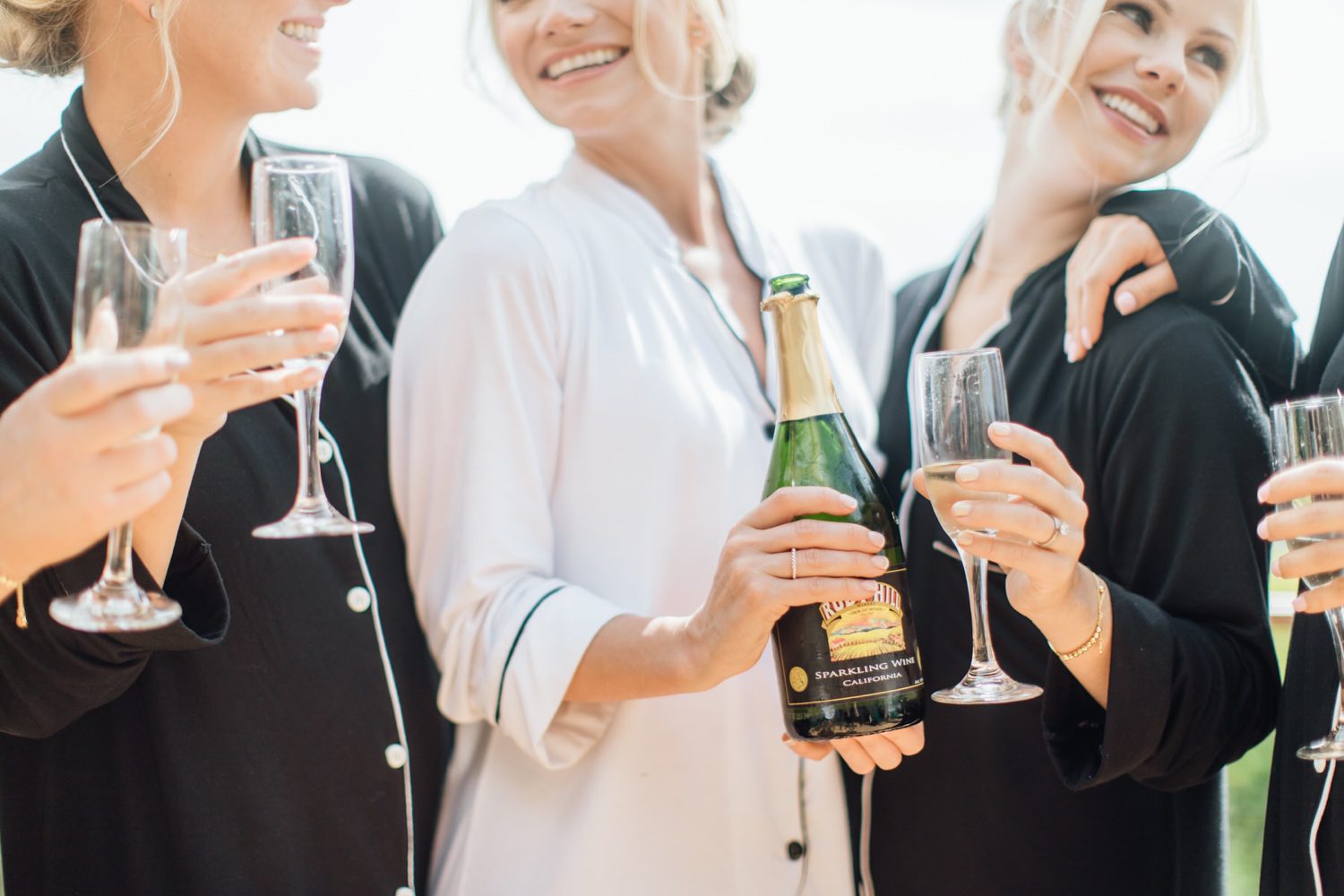 Bride drinking sparking wine with her bridesmaids dressed in matching black and white robes