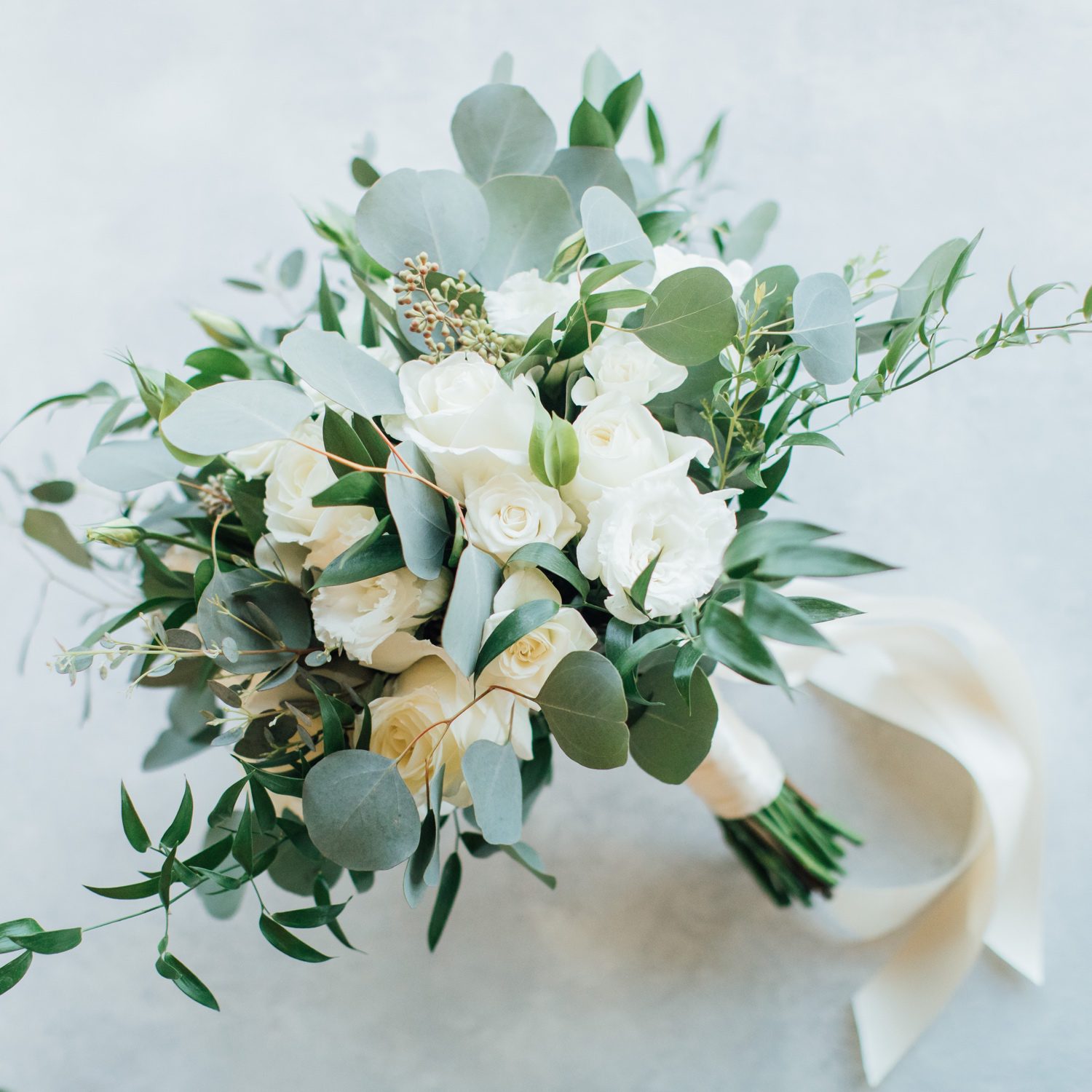 Wedding bouquet created with white roses and green foliage.