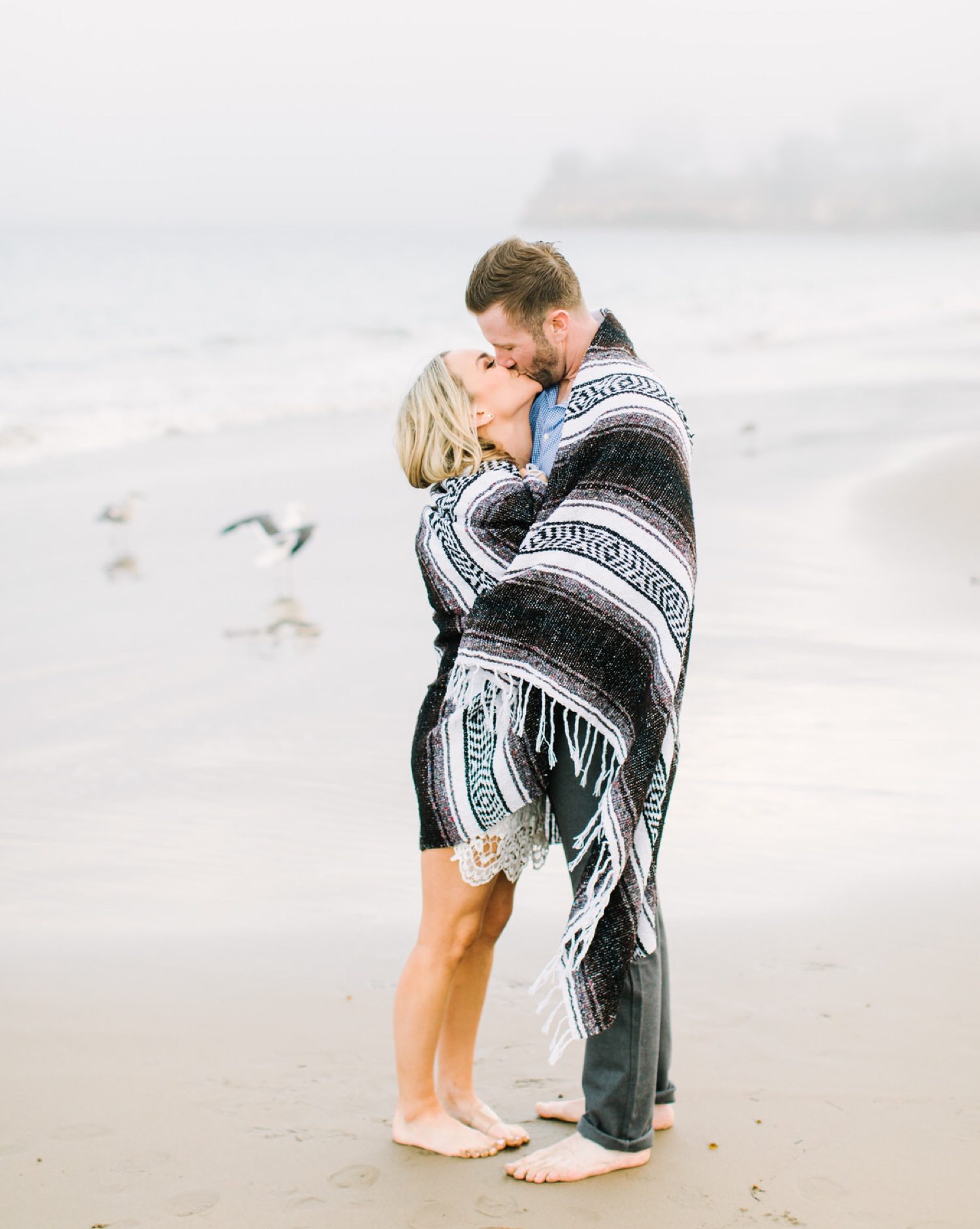 Couple wrapped in blanket while kissing on the beach