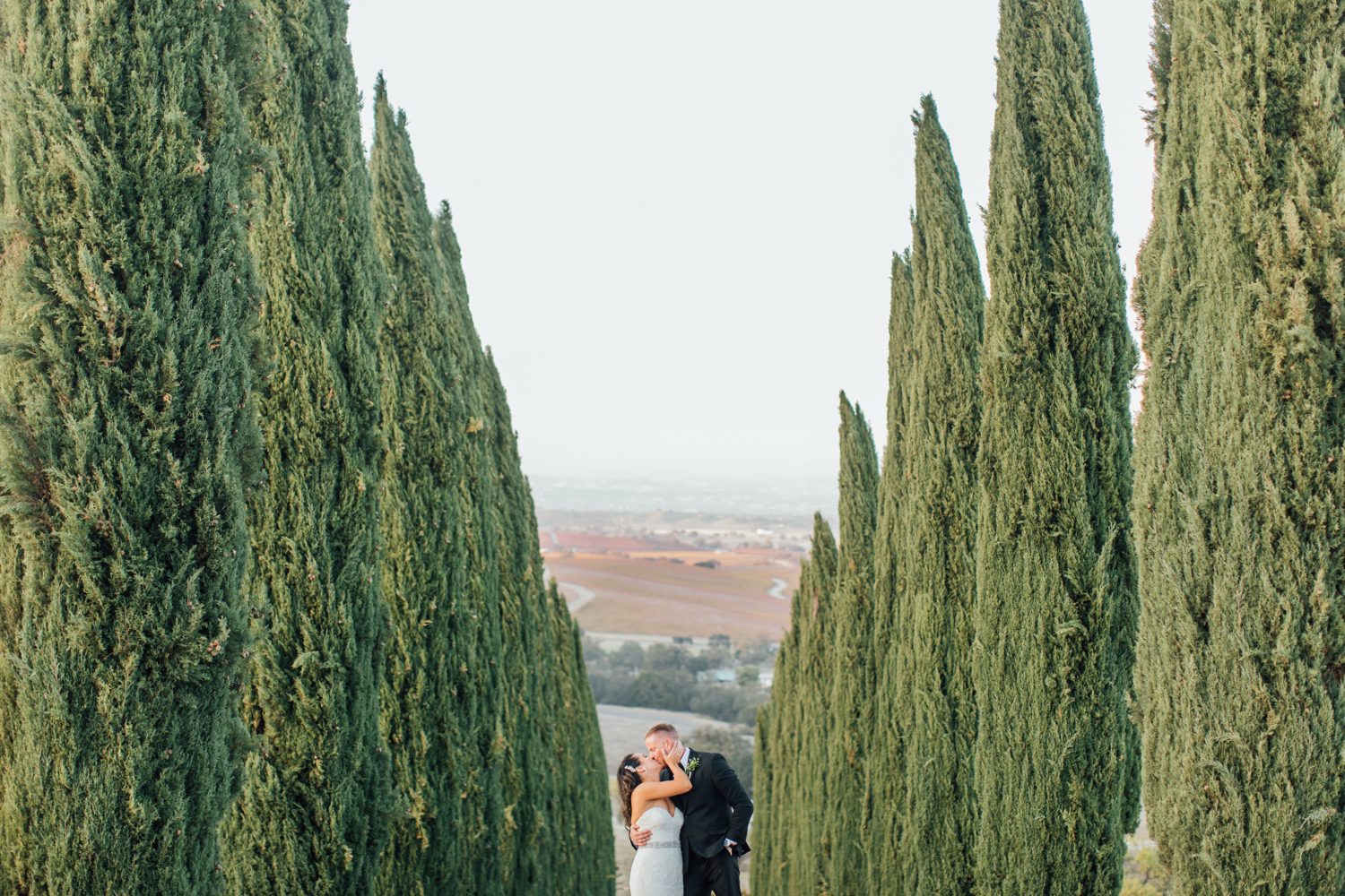 Bride and groom in front of cypress trees and view of Tuscany at european chateau inspired wedding in Paso Robles by photographer Jessica Sofranko