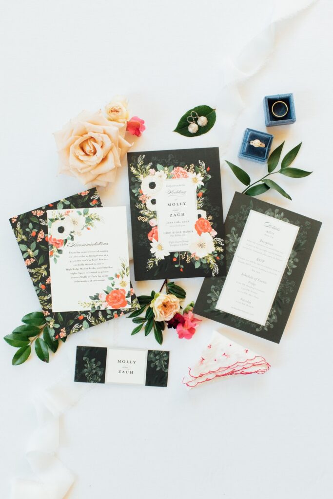 Wedding flat lay including wedding invitations, florals, and the bride and groom's rings.